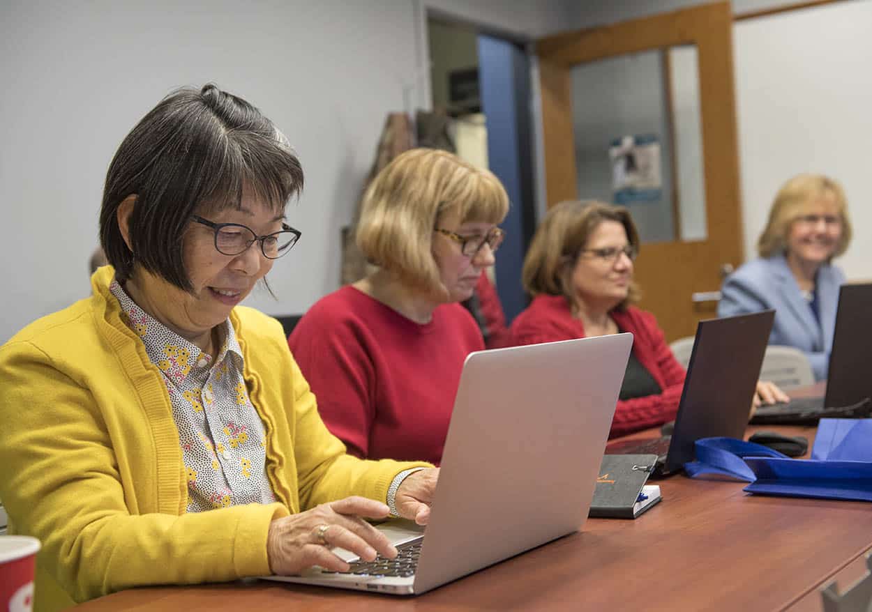 Several faculty members sit at a table looking each at their laptop computers.